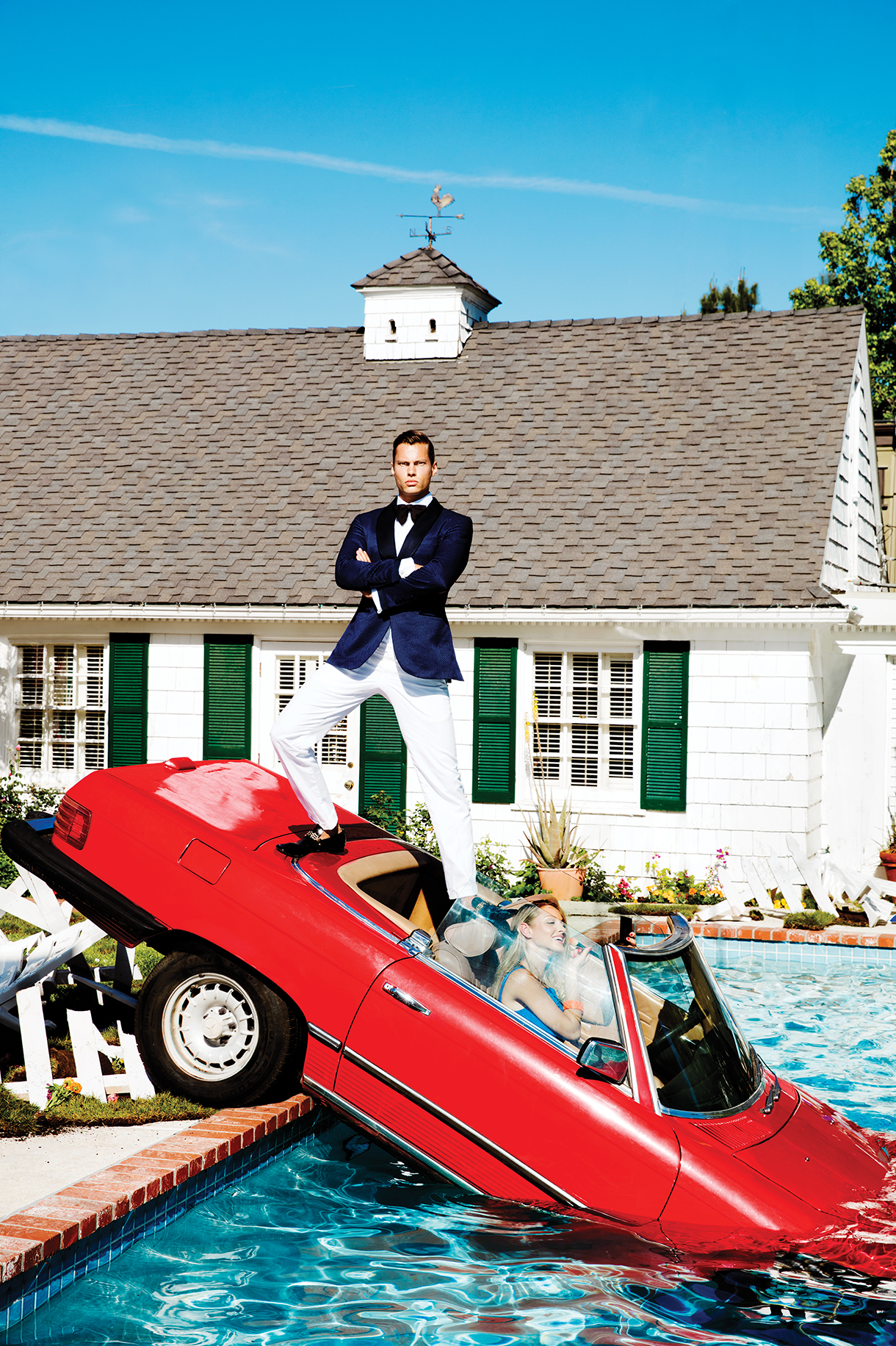 Red sports car with pretty woman driving in a pool with handsome man standing on car